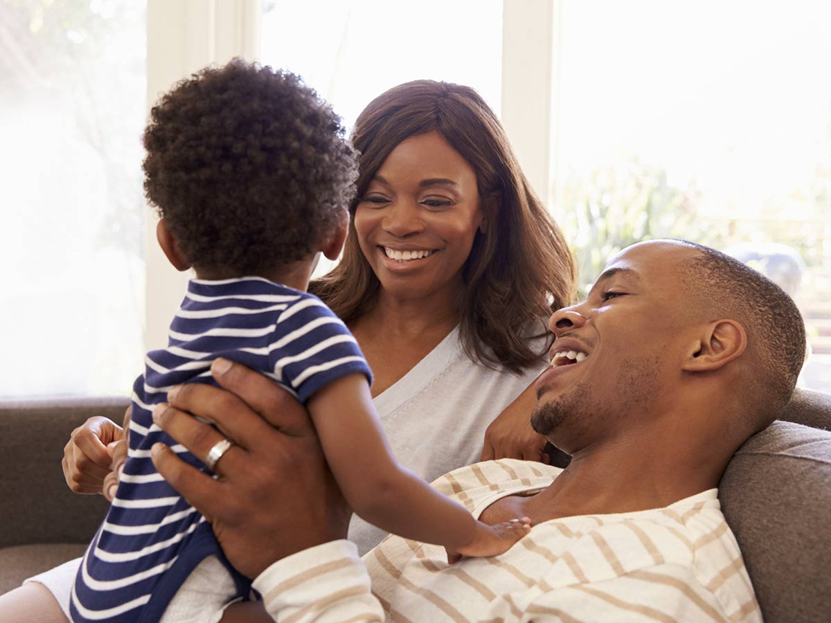 Couple is sitting on a couch holding their small child.