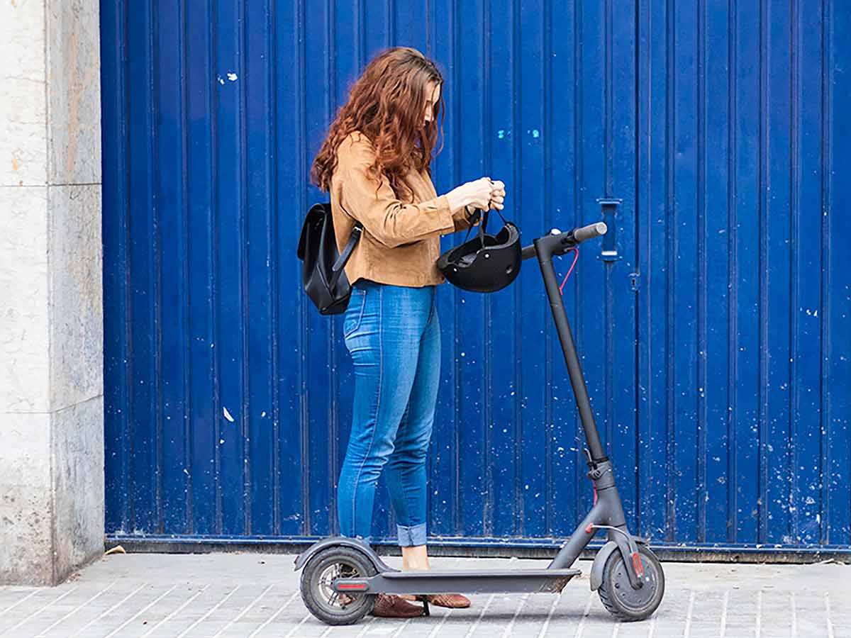 Mid-twenties male and female riding e-scooters side by side down a pedestrian roadway.