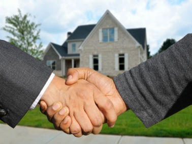 two people shaking hands in front of a house